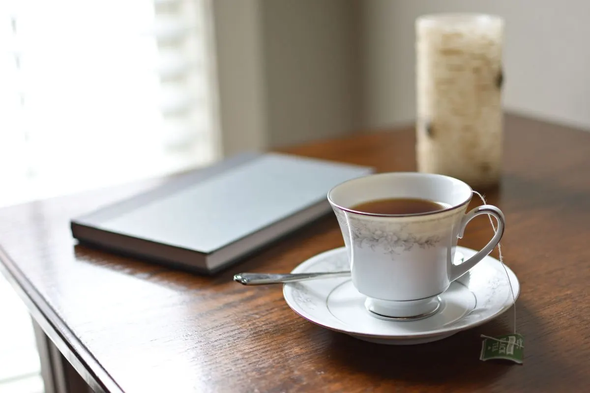 A cup of tea, a notebook, and a candle on a wooden table