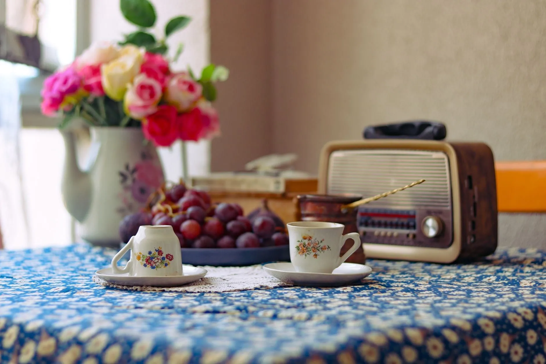 A vintage radio on a kitchen table with cups and flowers
