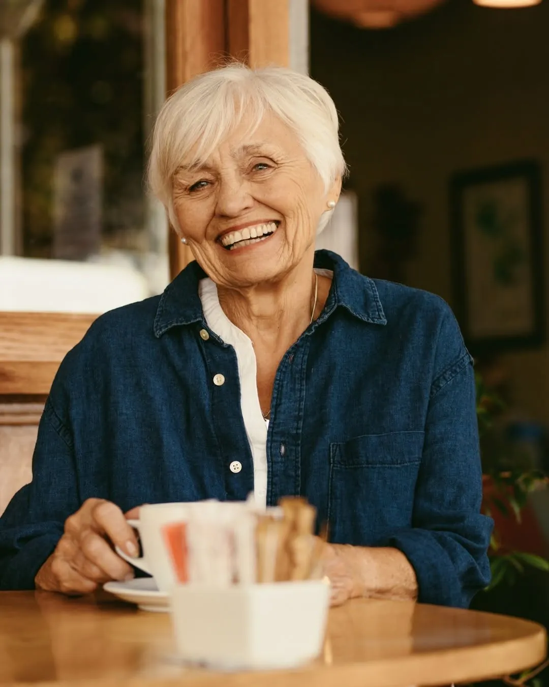 A smiling older woman with a cup of coffee at a café table