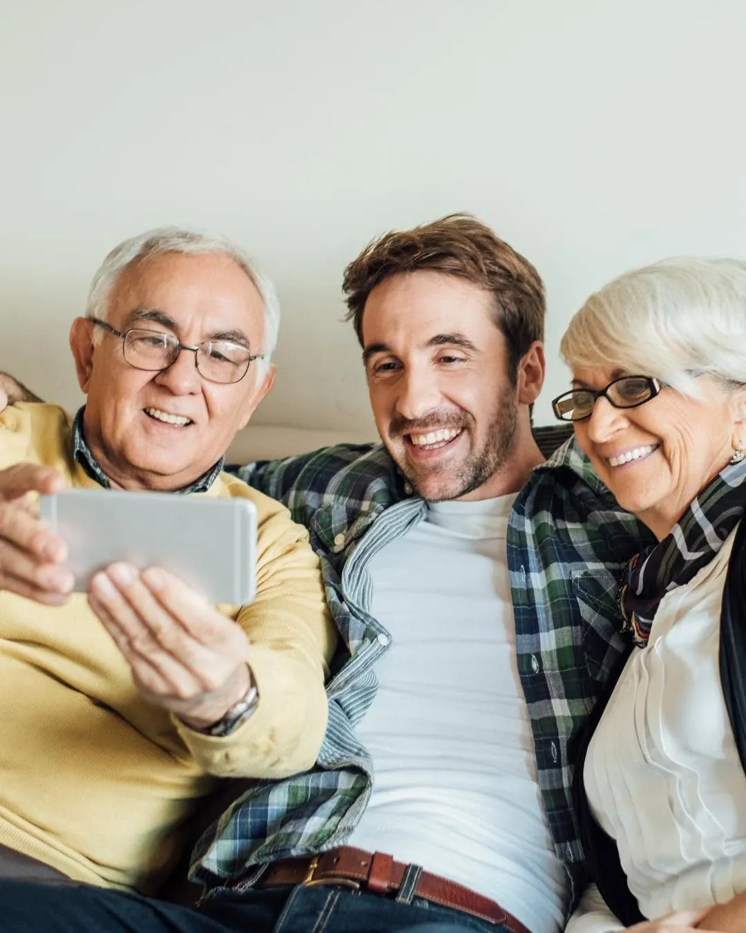 An older couple and a younger man laughing at a phone on the couch