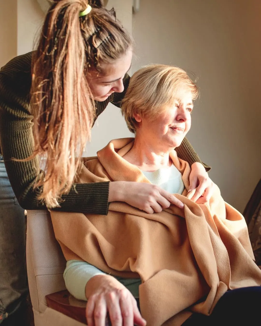 A young woman tucking a blanket around an older woman in her chair