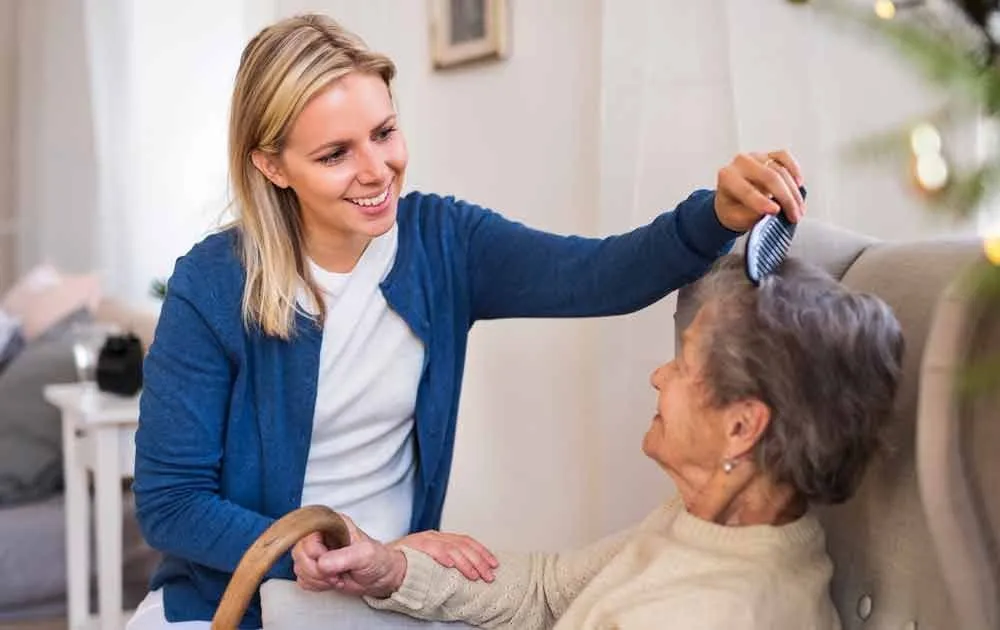 A caregiver brushing an older woman's hair at home