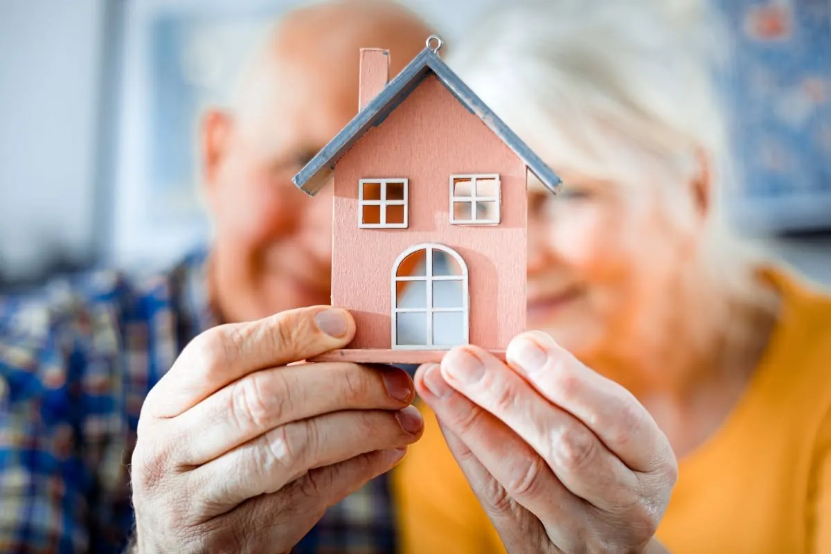 Two older hands holding a small model house