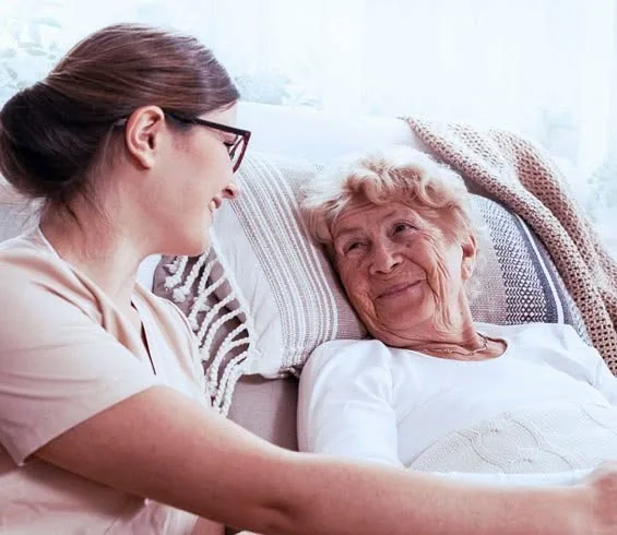 A caregiver talking with a smiling older woman resting in bed
