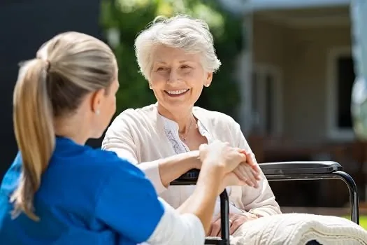 A caregiver holding hands with an older woman in a wheelchair outside